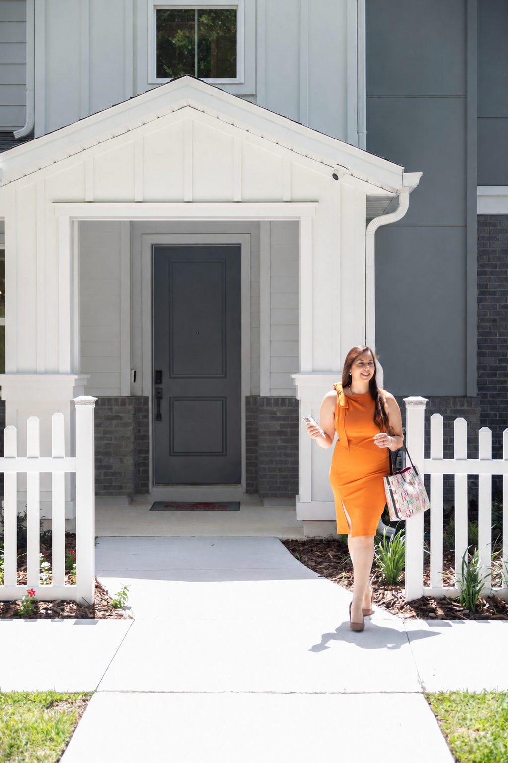 Sheryl Cury caminando hacia la cámara frente a una casa nueva con cerca blanca